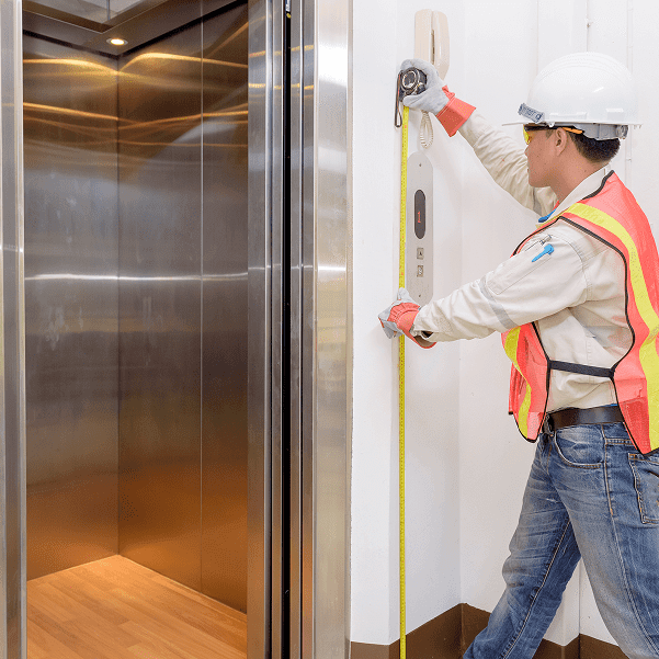 Technician measuring beside open elevator door.