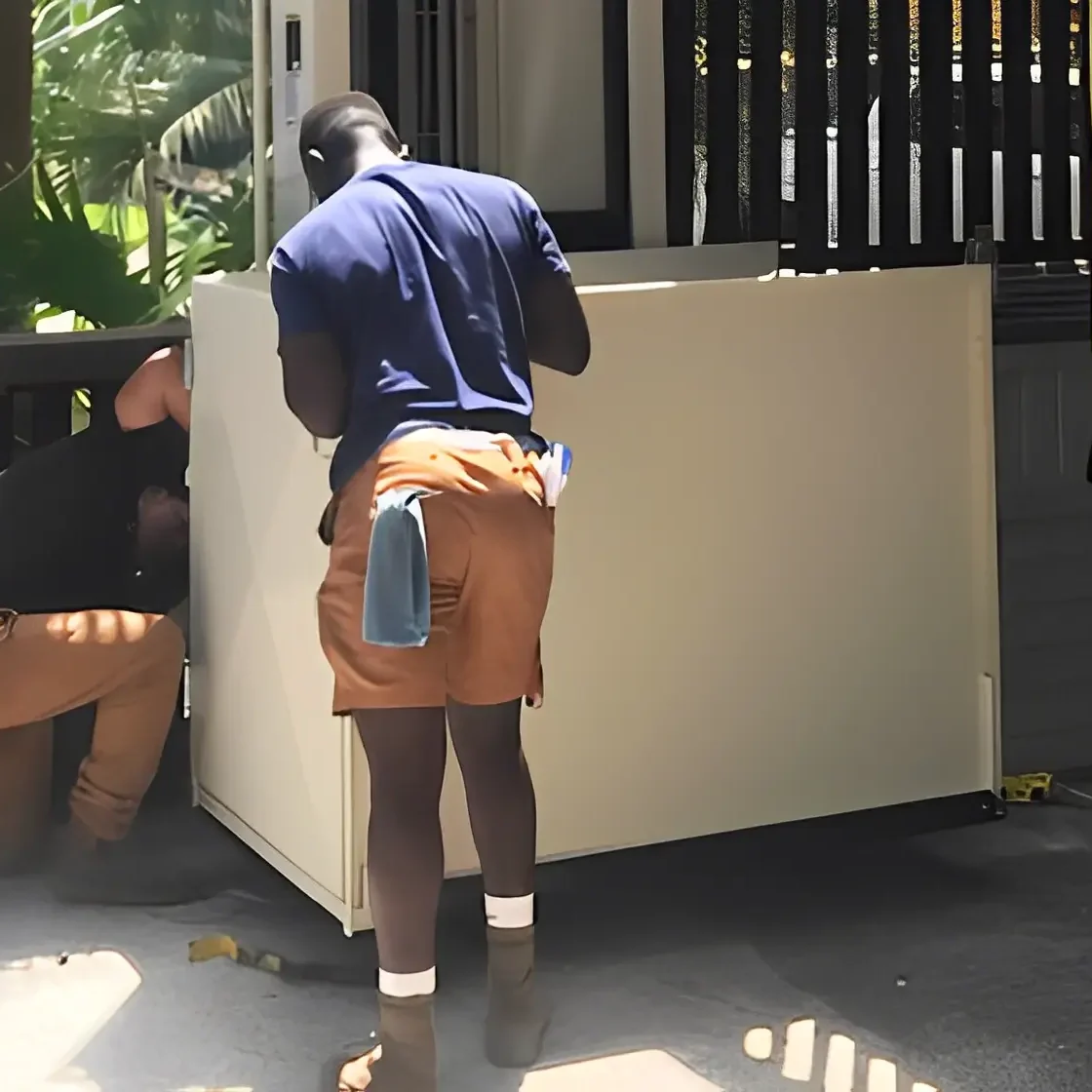 Workers installing large white appliance outdoors.